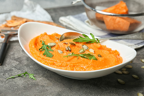 A freshly made pumpkin mash recipe in a white bowl, topped with green herbs