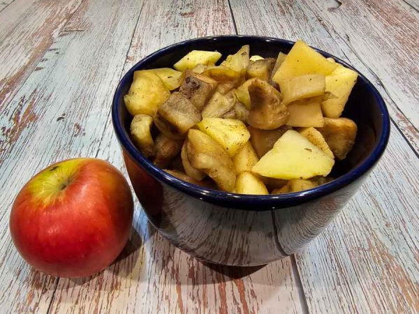 A bowl of sauteed apple eggplant with cinnamon next to an apple.