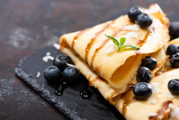 Folded coconut flour crepes topped with blueberries and a drizzle of syrup