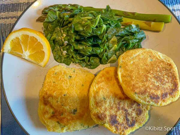 3 gluten-free salmon patties with a side of green vegetables and a wedge of lemon on a plate