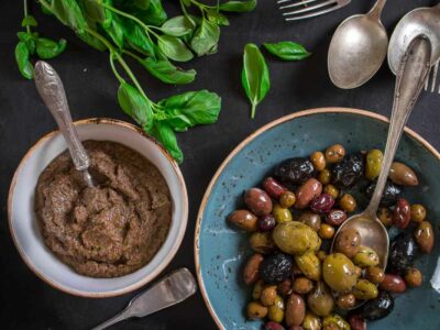 Homemade vegan olive tapenade alongside a bowl of mixed olives. Both with spoons, ready to serve