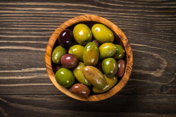 Olives assortment in wooden bowl on dark wooden table. 