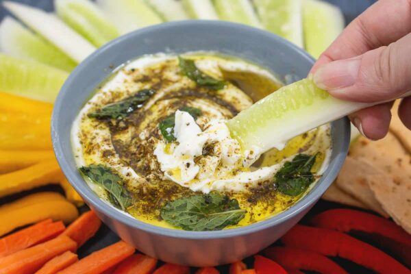 A hand dipping a celery stick in to a bowl of zaaaar labneh