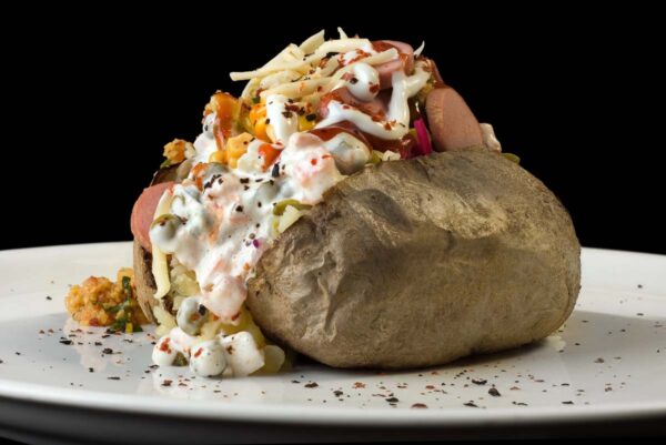 Stuffed baked potato with cheese, hot dogs, vegetables, and ranch dressing